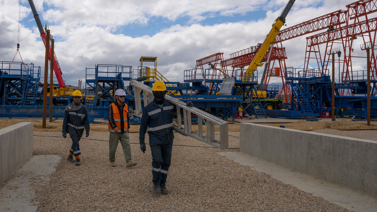 Tres trabajadores del Metro caminando en el patio taller con las estructuras del patio de prefabricados de vigas U en el fondo