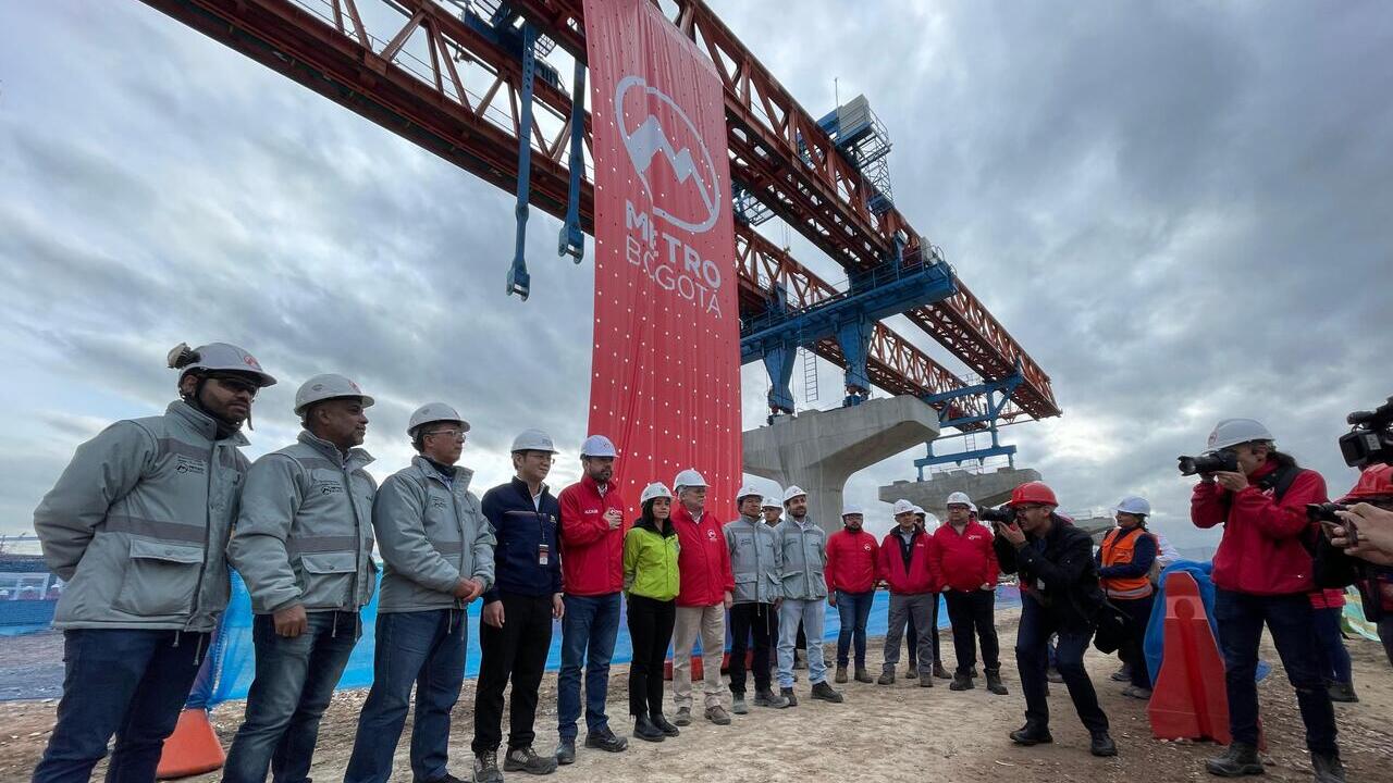 El alcalde y los invitados especiales del evento posan debajo de la viga lanzadora que tienen un pendón con el logo del Metro de Bogotá