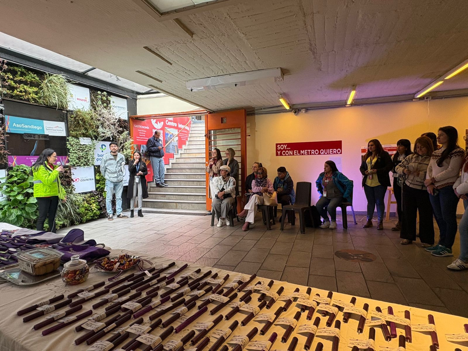 La galería subterránea con varias personas en su inauguración, se ve el jardín vertical a la izquierda, las mesas con la exposición y varios asistentes