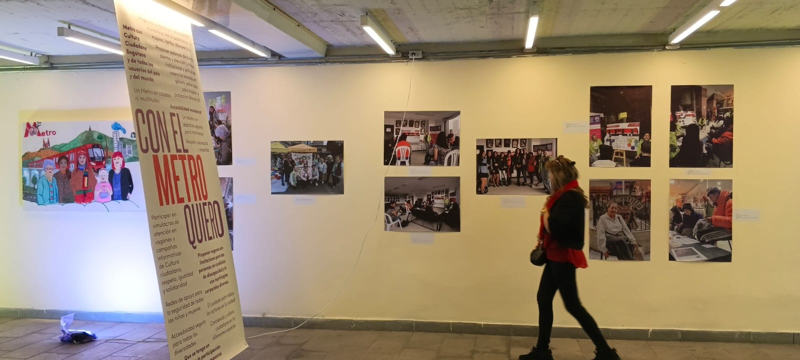 En el fondo: Pared de la galería donde se ven varias fotos. Delante se ve una mujer caminando viendo las fotos