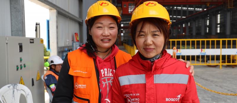 Las dos operadoras chinas sonriendo en el patio de prefabricados del Metro de Bogotá